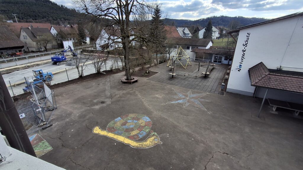 geteerter Schulhof mit Baum und Kletterelementen