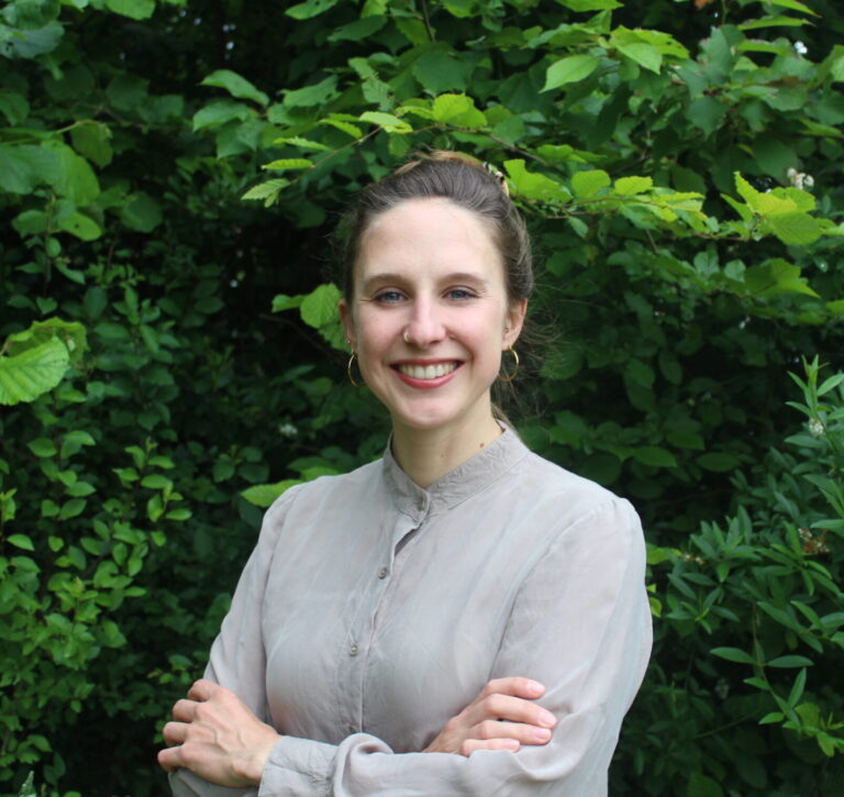 Anna-Lena Stettner steht vor einer grünen Hecke