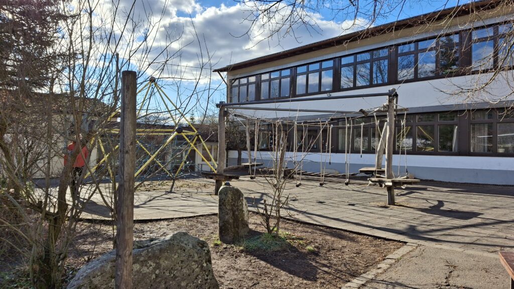Niedrigseilparcours vor Schulgebäude, darunter Gummiplatten