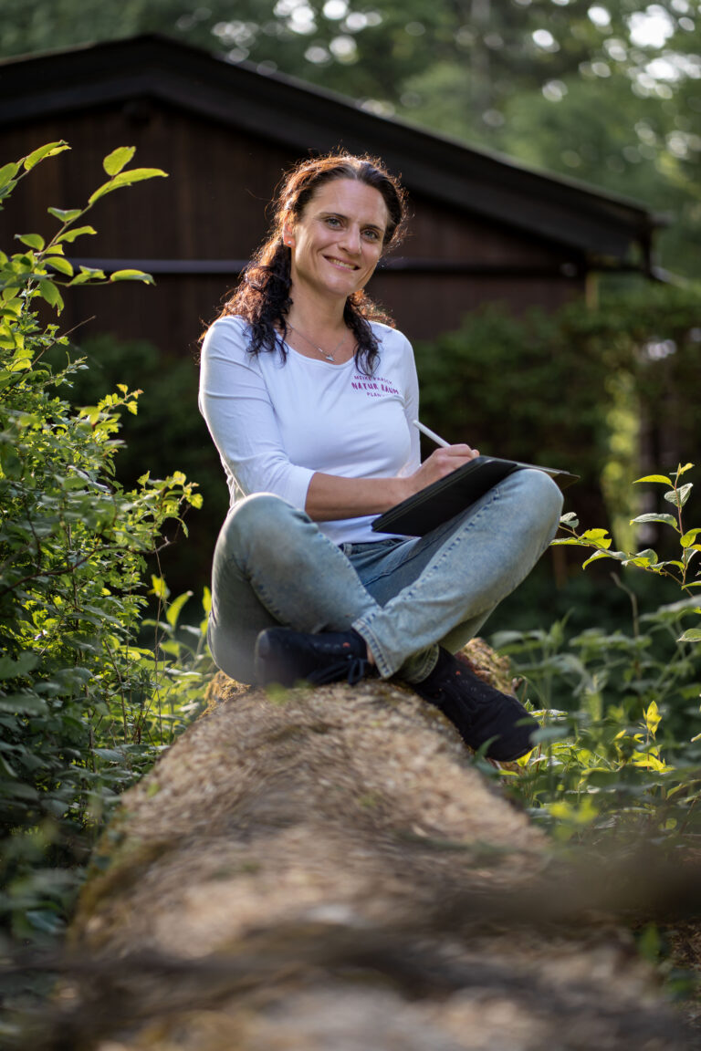 Meike Paasch sitzt auf einem Baumstamm im Garten