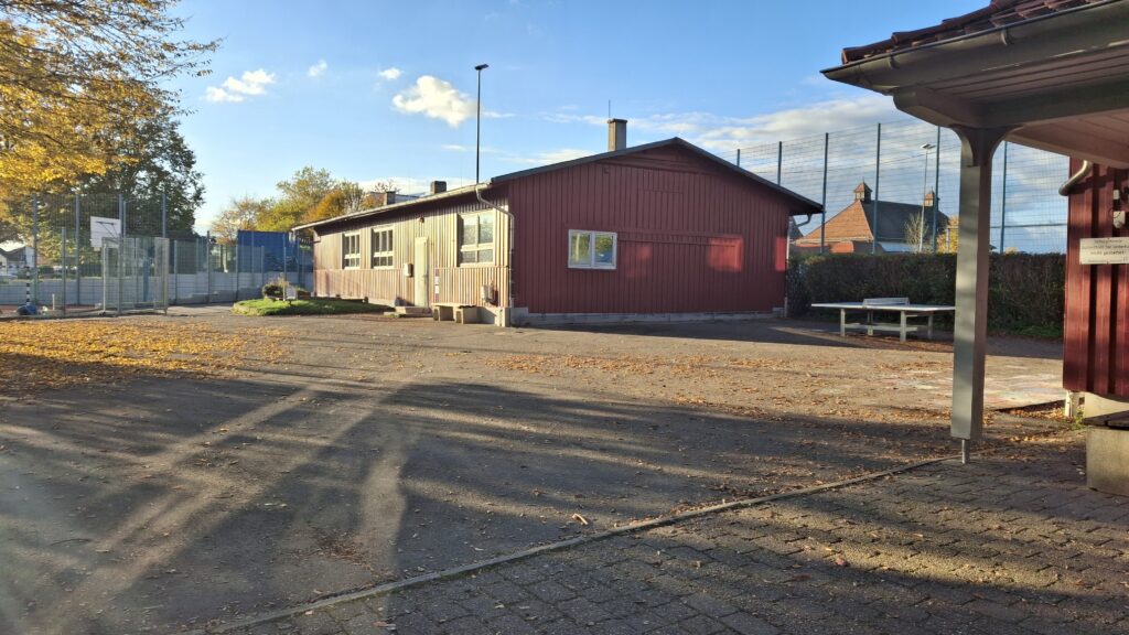 geteerter Schulhof, im Hintergrund ein Gebäude und Sportplatz