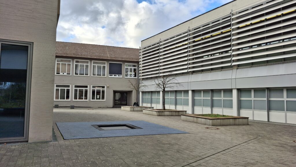 gepflasteter Innenhof, mit Bodentrampolin und zwei Bäumen ohne Blätter