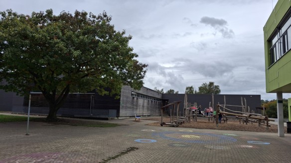 gepflasteter Hof, im Hintergrund ein Kletterelement aus Holz mit Schüler:innen