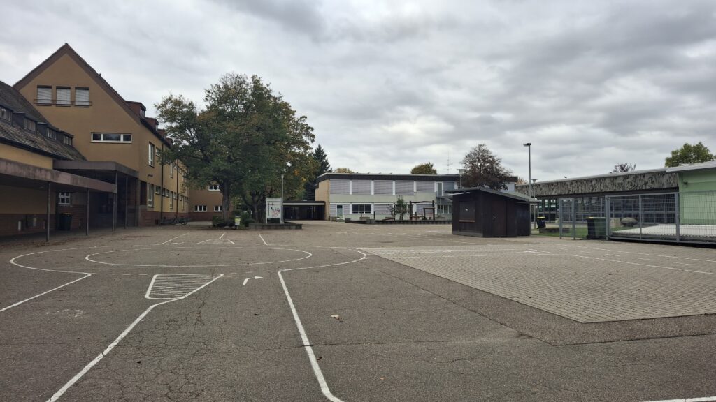 geteerter Innenhof mit Schulgebäude und vier Bäumen