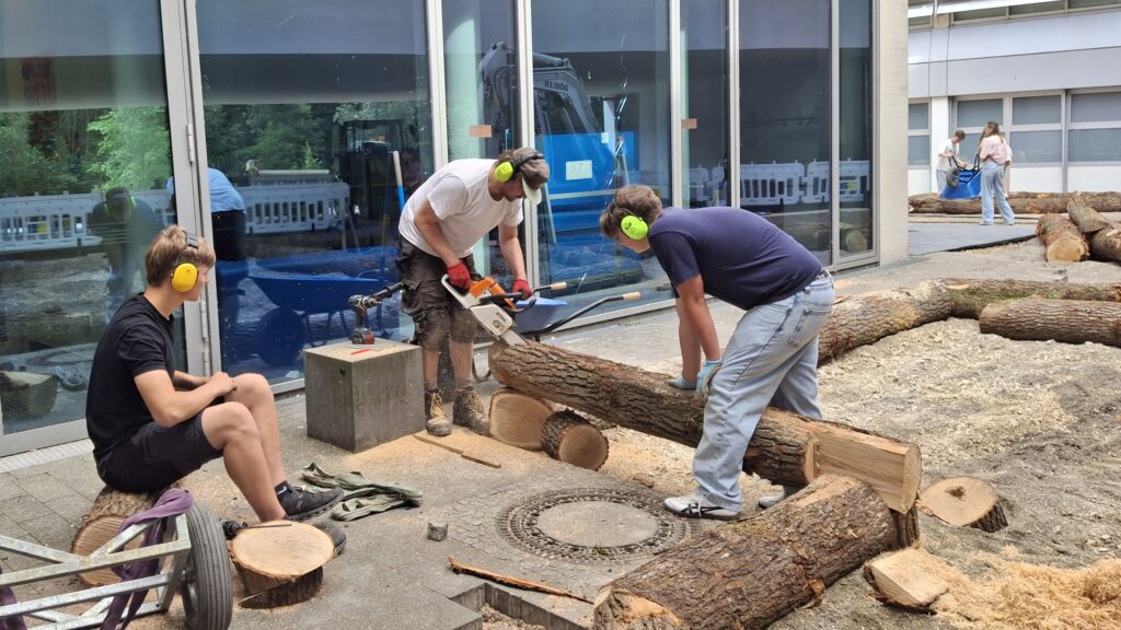 Drei Jungs bearbeiten Holzstamm mit einer Säge